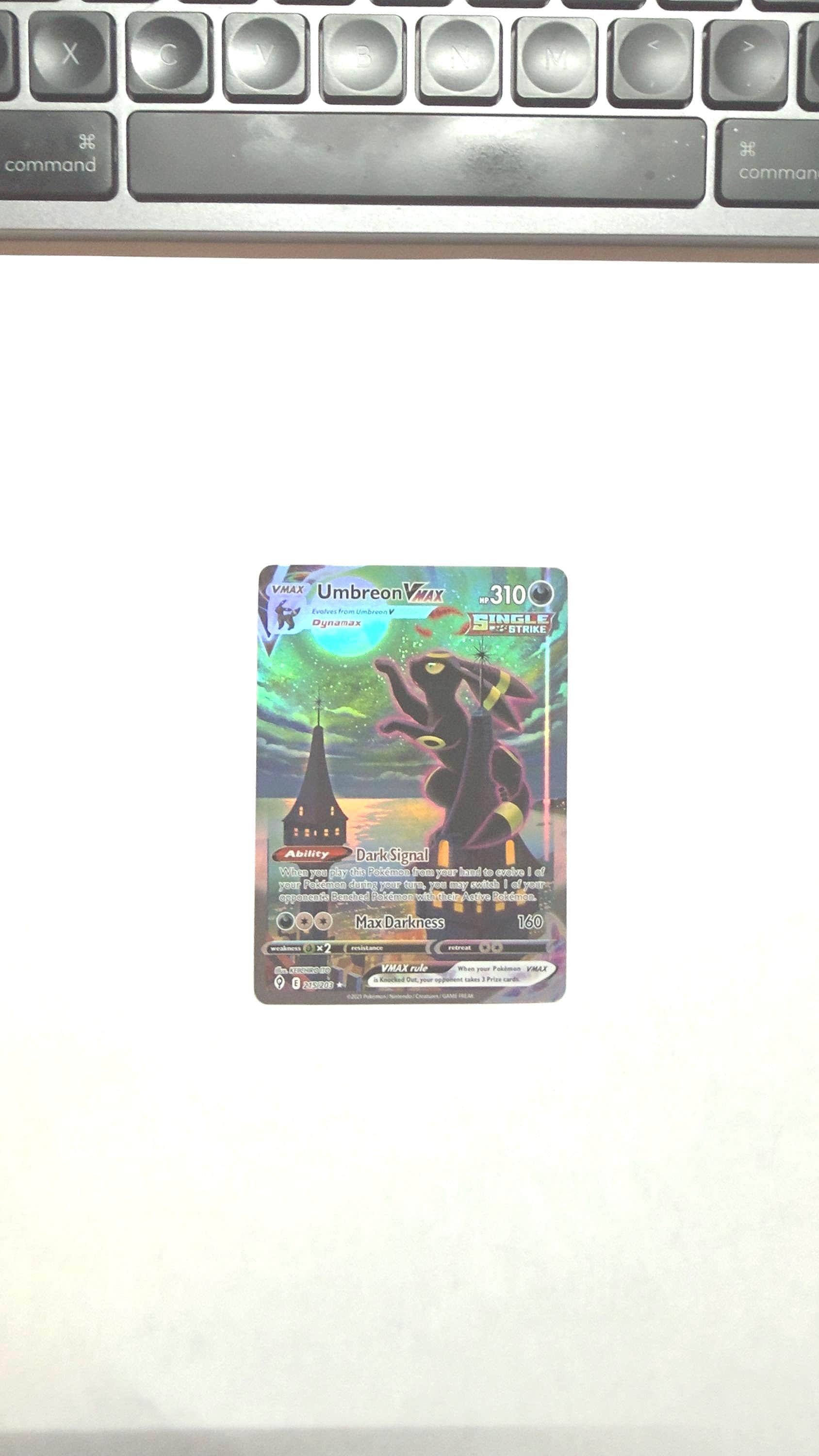 May include: A Pokémon trading card featuring Umbreon VMAX. The card has a dark color scheme with a silhouette of Umbreon against a night sky. The card includes text such as "Dark Signal" and "Max Darkness".